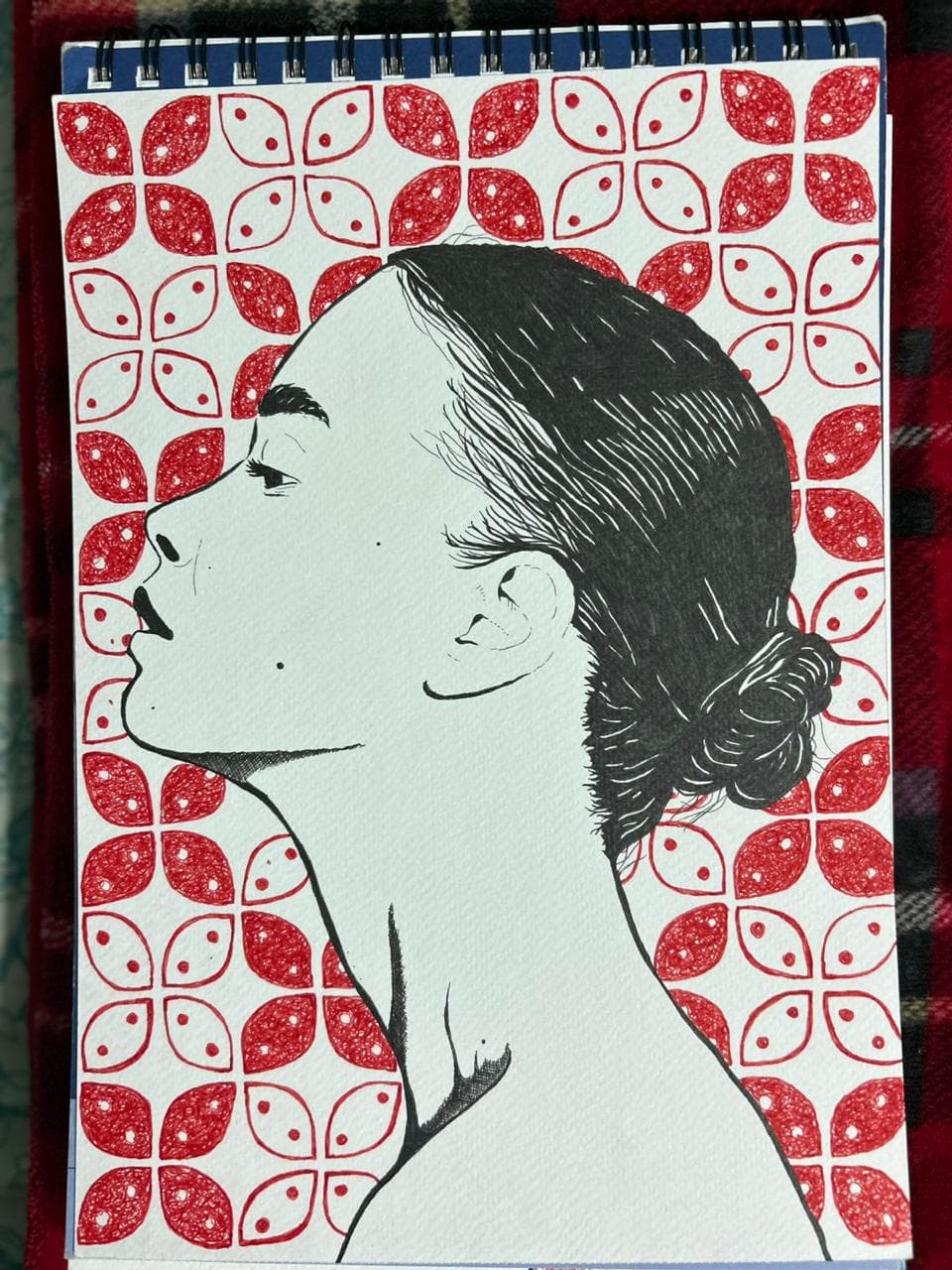 Ink profile portrait of a young woman with a low bun, set against a hand-drawn red four-petal tile pattern.